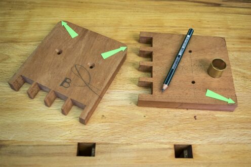 2 sections of mahogany with drilled holes in the centre of each, with a pencil and curved tool for rounding corner edges.