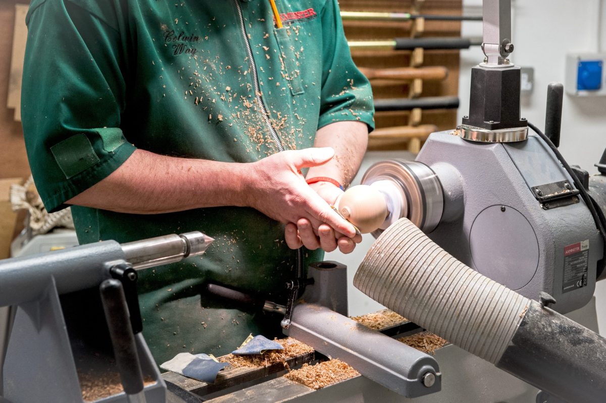 Sanding the top section of the pepper mill on a lathe.