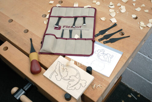 Flexcut carving kit on workbench with template and wood held in a vice